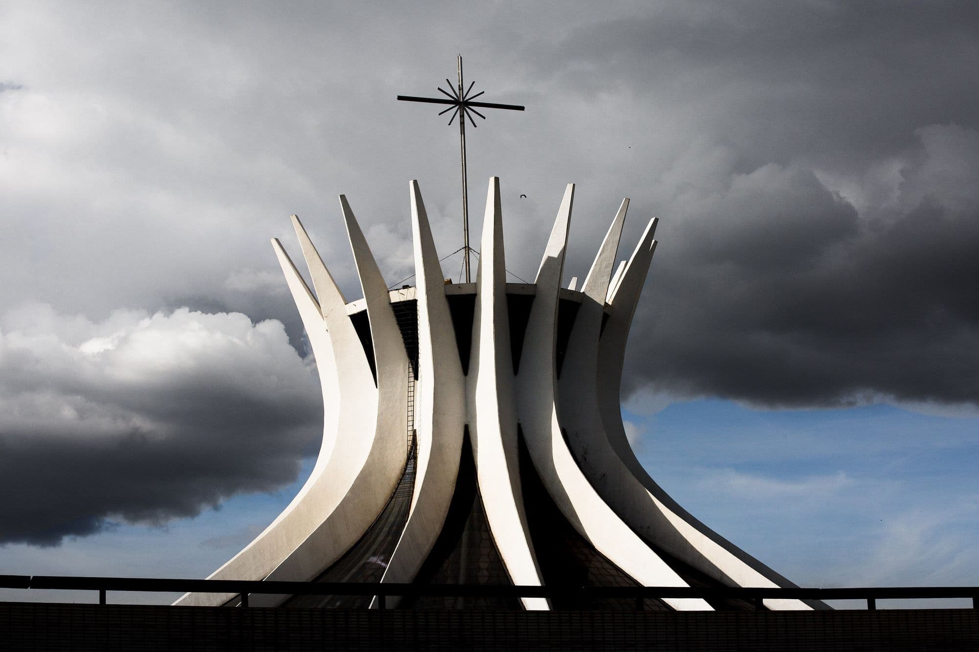Catedral Metropolitana de Brasília, com as colunas de concreto branco contra um céu de nuvens carregadas.